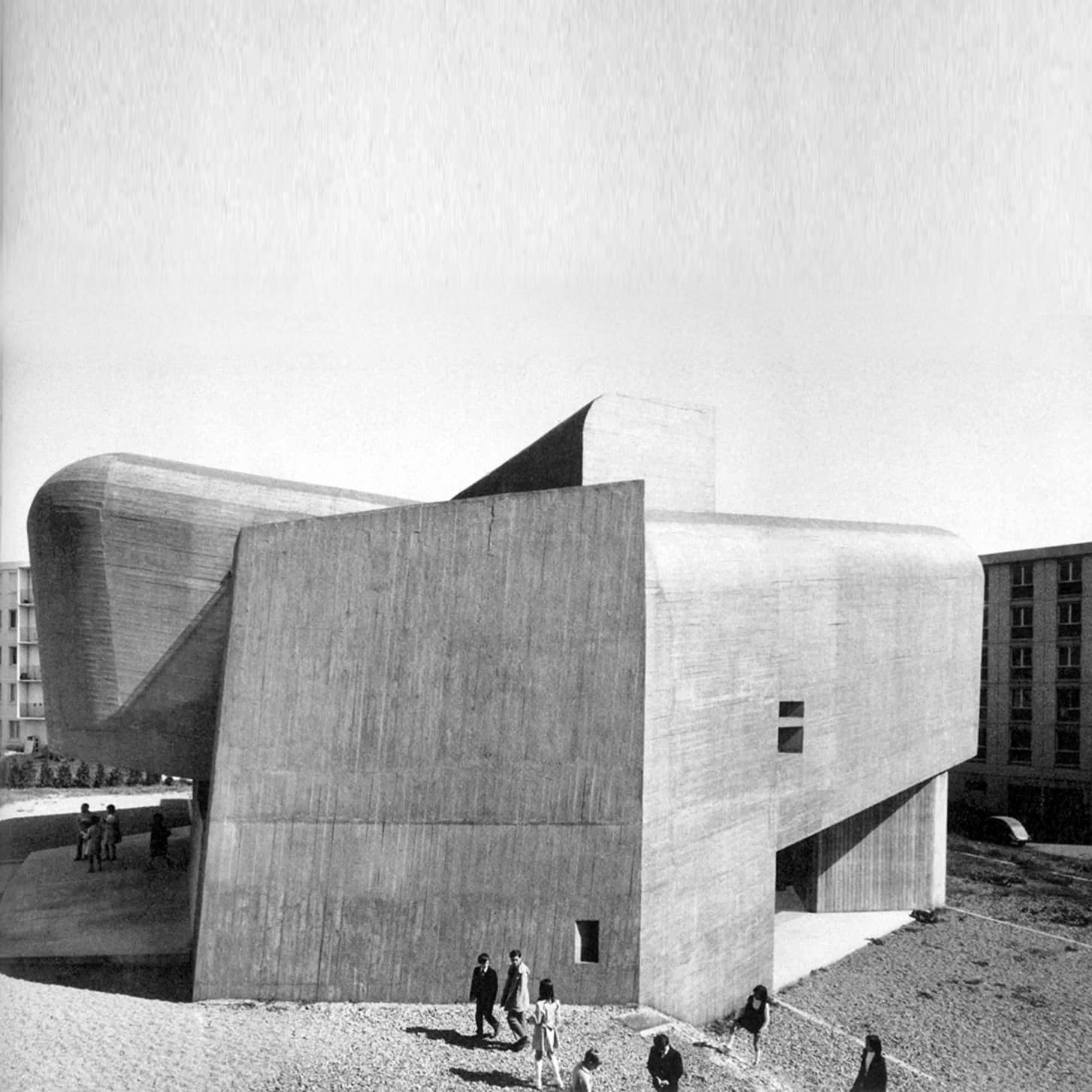 The church of Sainte-Bernadette du Banlay at Nevers: two board-marked concrete shells split and pushed apart above a low entrance, and inside, a windowless nave whose floor slopes in two ramped halves toward a low point, lit only where the shells fail to meet.