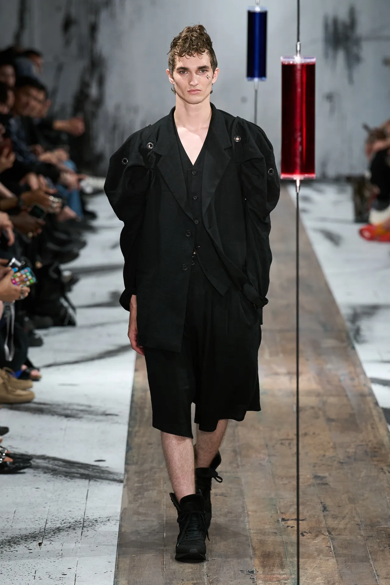 A Yohji Yamamoto runway look: layered black tailoring cut loose from the body, asymmetric hems, the silhouette carried by the volume of cloth rather than the figure inside it.