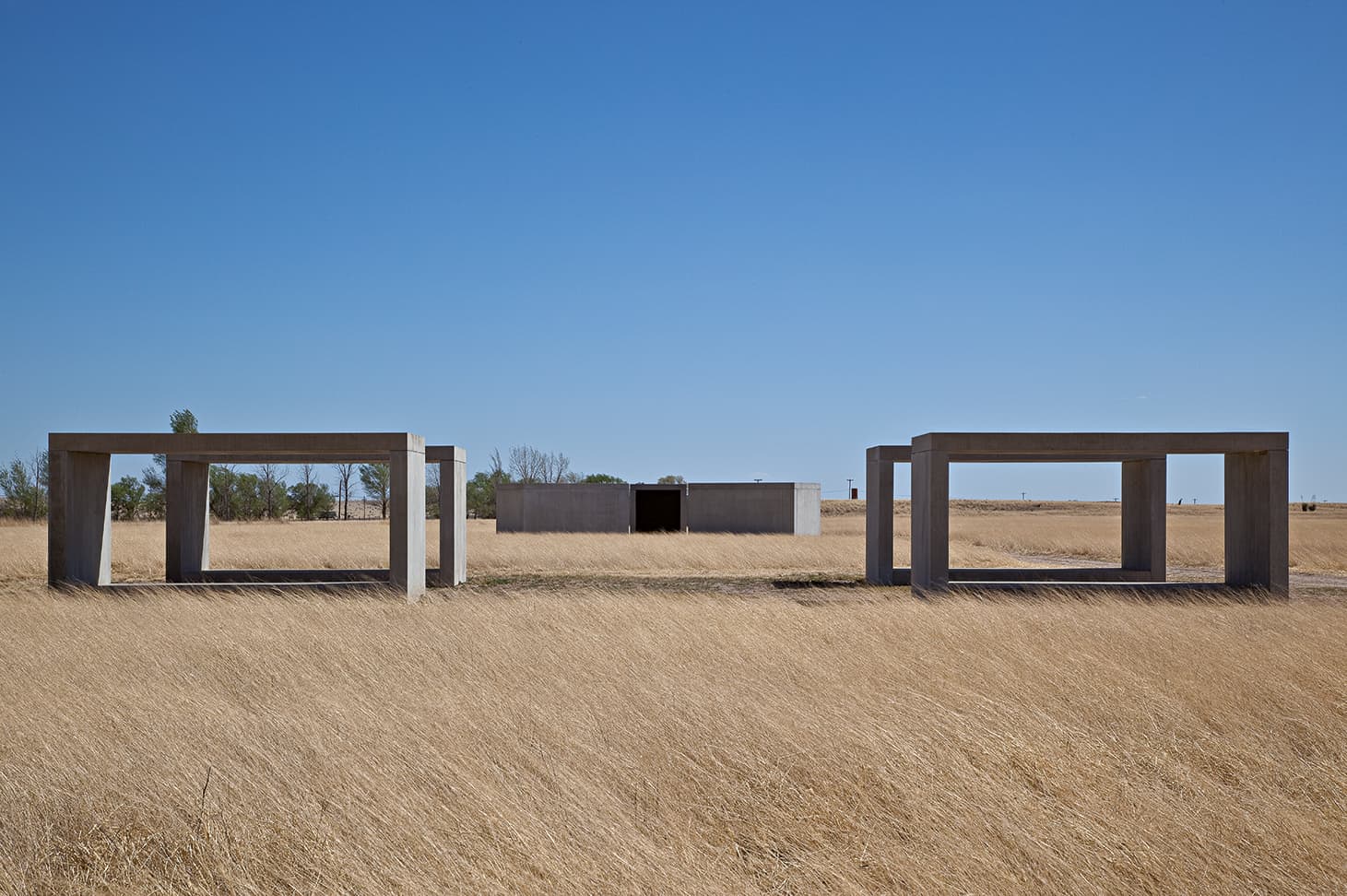 Donald Judd's concrete units standing in the grass at Chinati, open boxes of the same dimensions spaced along a line under an empty sky, with archival photographs of them being cast and assembled on site.