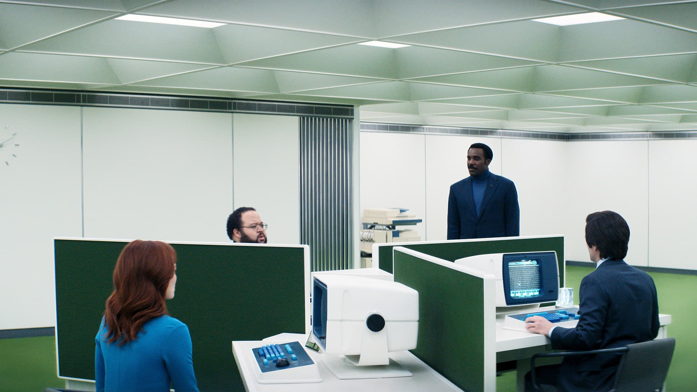 The Lumon office floor from Severance: deep green carpet, white walls, four small desks with boxy terminals in an otherwise empty room.