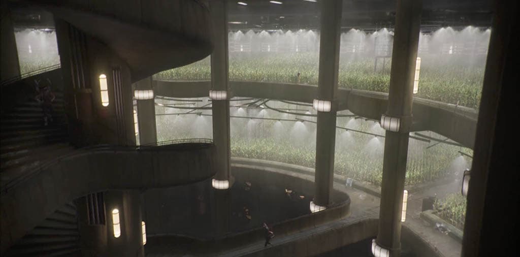 A level of the silo set: open steel bridges crossing the central shaft, lit from the walls, with the stair winding down out of frame.