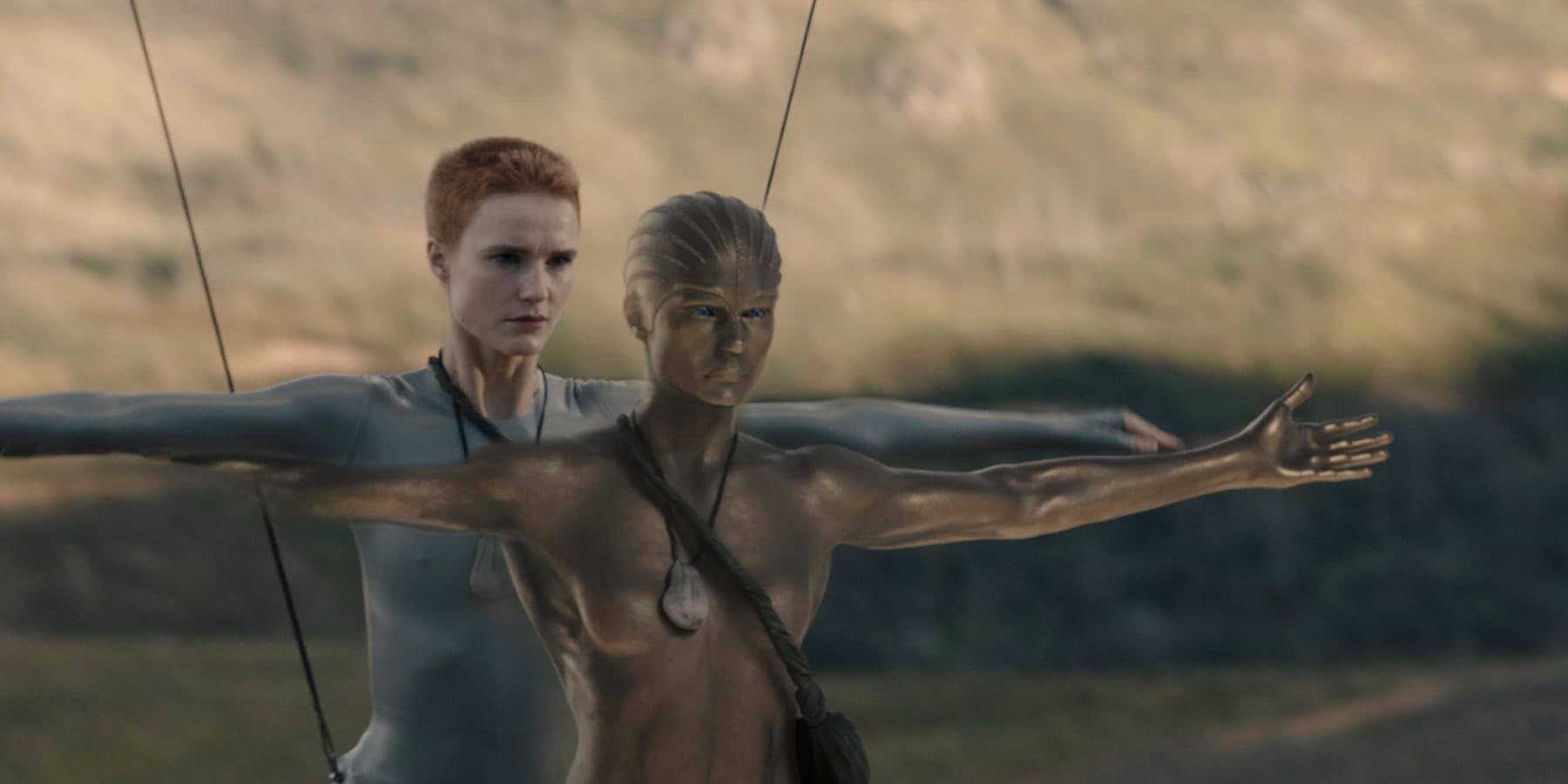 Two androids standing on the bare rock of Kepler-22b, pale and unmarked against a grey sky.